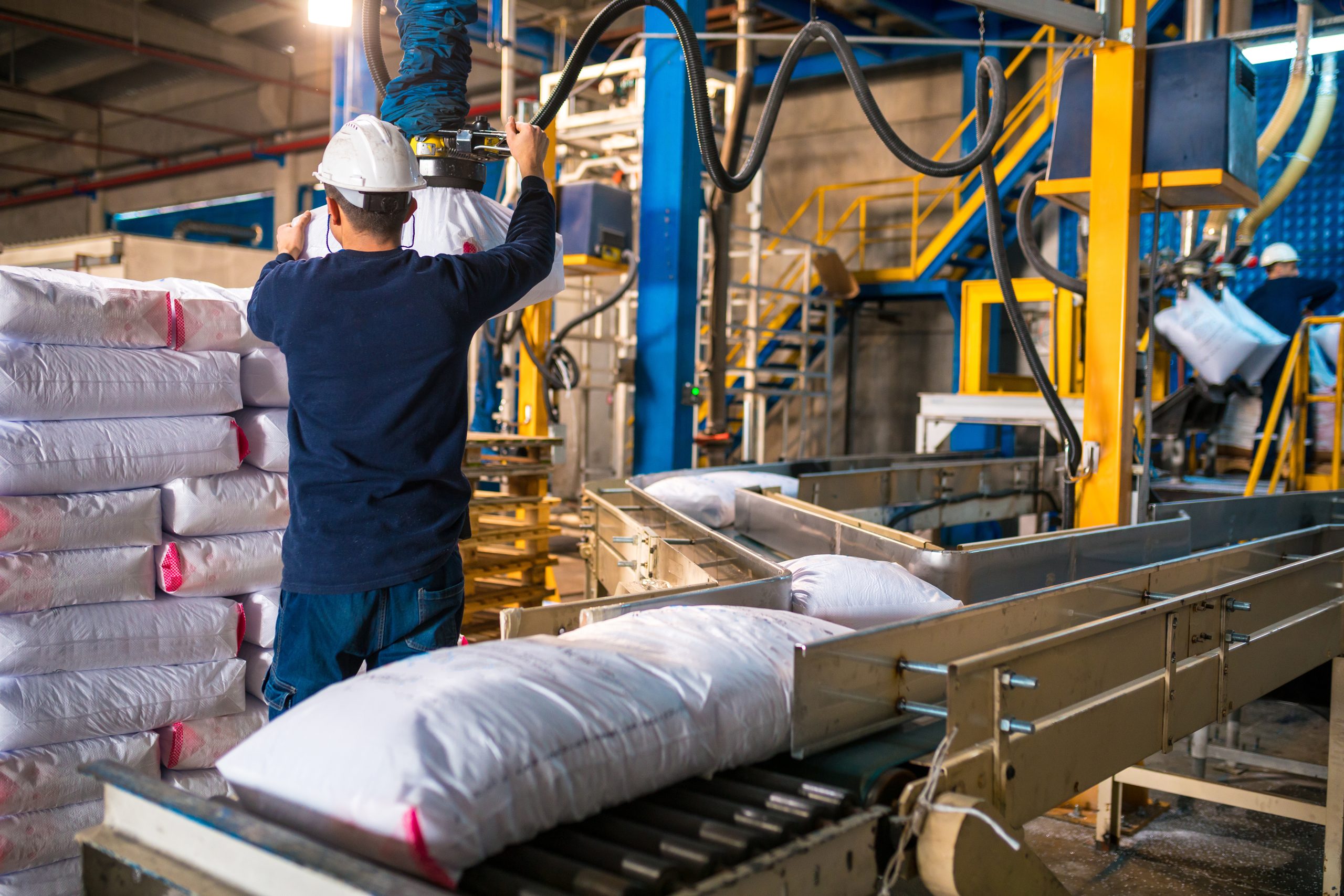 Workers loading rows or stacks of white sack bags from the conveyor belt and organizing them on the side at a large warehouse. PAR4012 Series Spec Sheet Use in Material Handling | Ultrasonic Transducers | Parsonicscorp.com | 815.338.6509